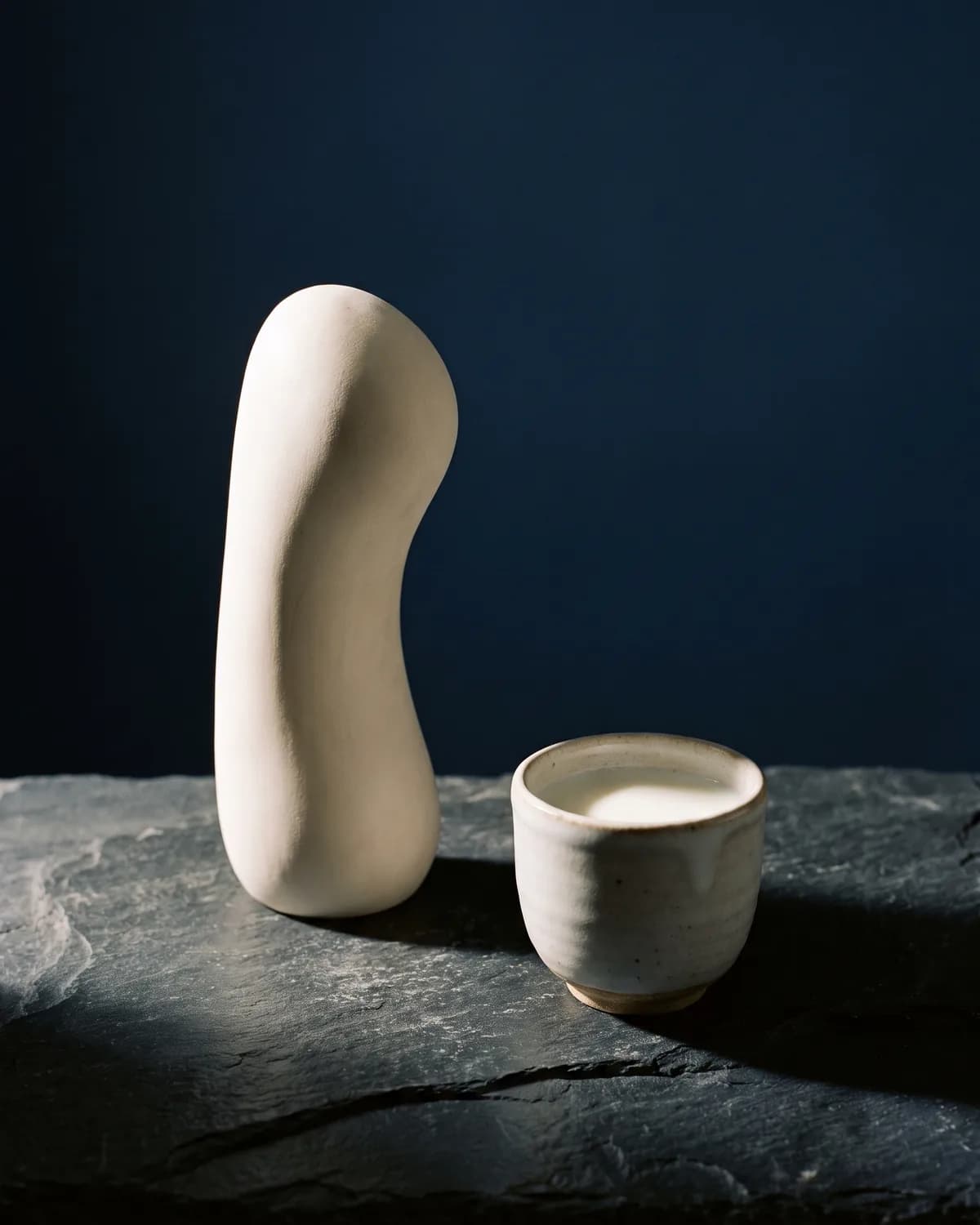 A smooth white sculptural form beside a cup of milk