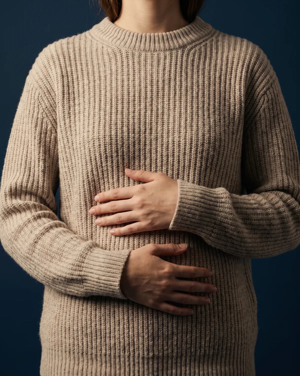 Hands resting gently on the stomach over a knitted jumper