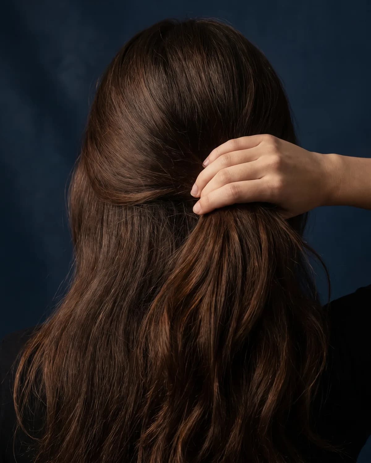 Long, healthy hair gathered in one hand, seen from behind