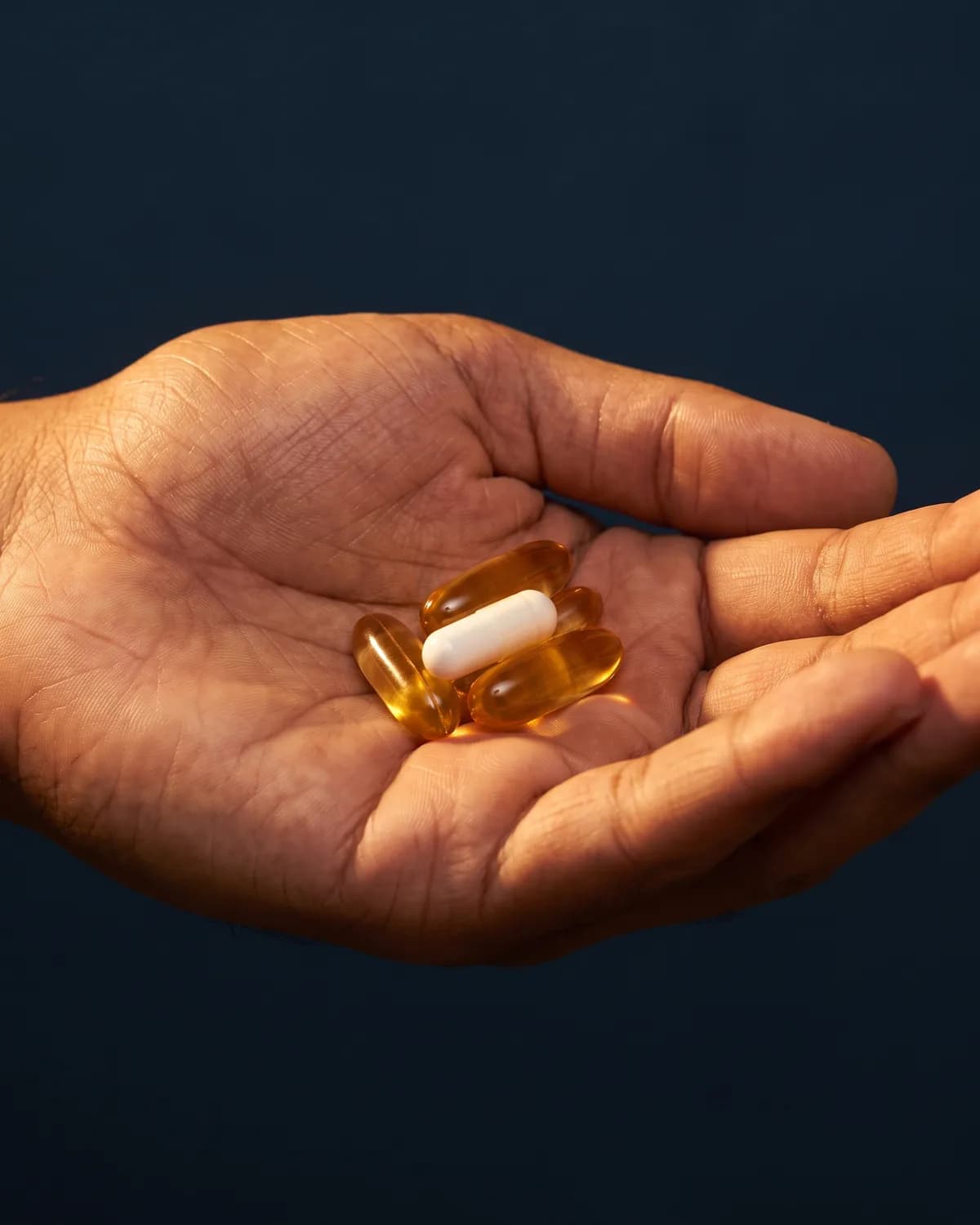 An open hand holding vitamin capsules in warm light
