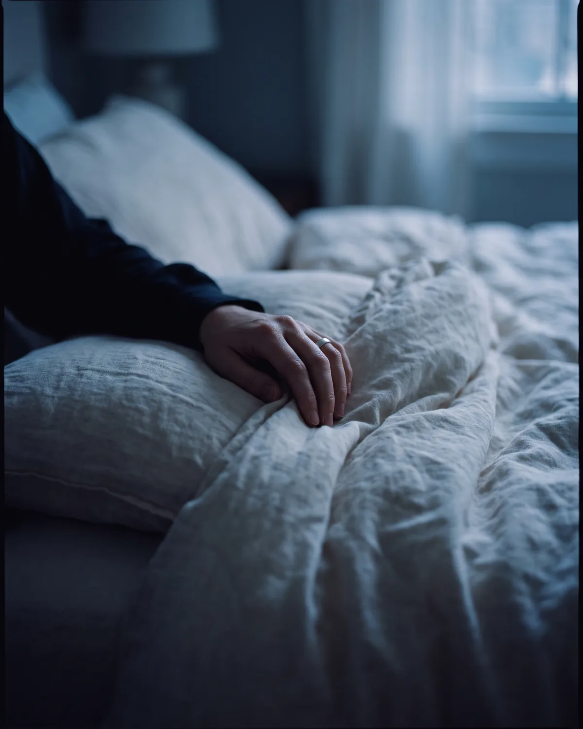 A relaxed hand on linen bedding in early-morning light